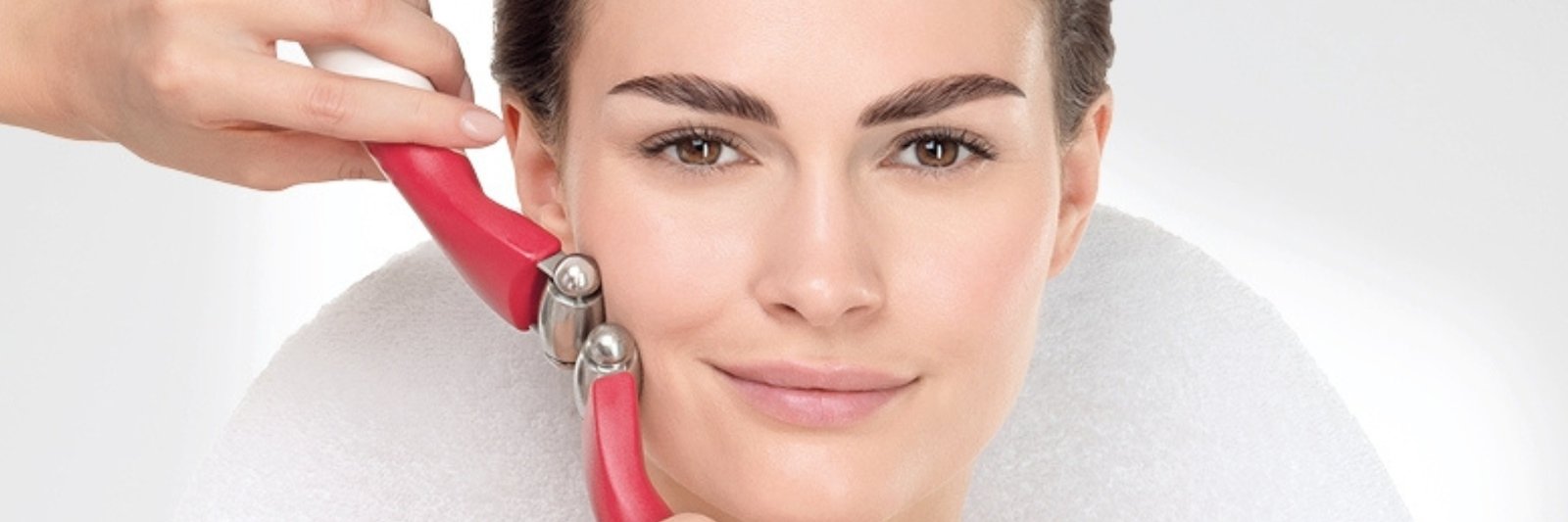 A woman receiving a Hydradermie Lift facial treatment with red microcurrent rollers applied to her cheek, illustrating a non-invasive face lift technique.